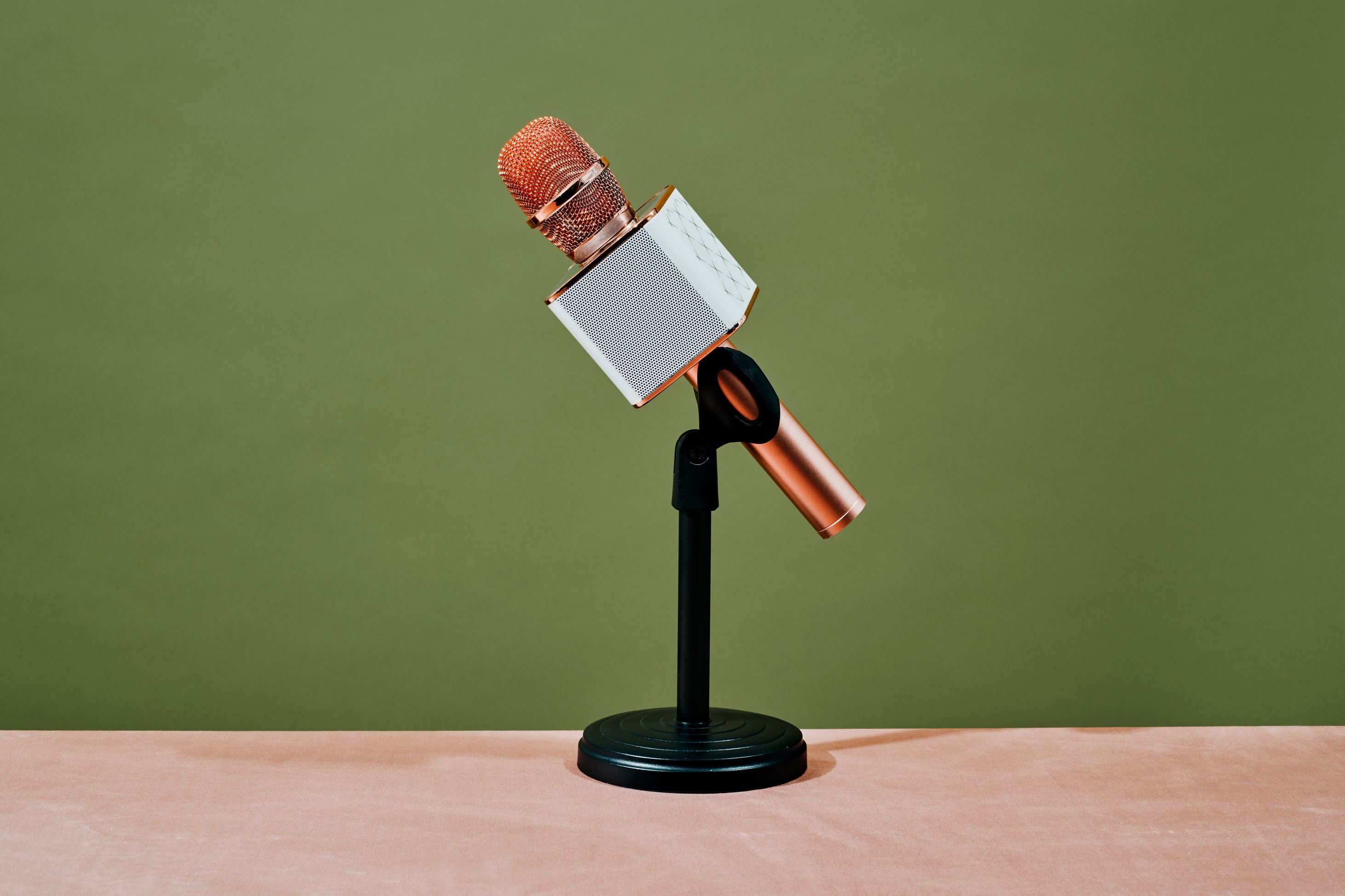  A wireless gold microphone on a black stand with a green background. 