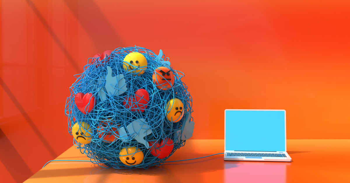 A blue wired ball with different emoji faces and thumbs up on it sitting beside an open laptop on an orange background. 